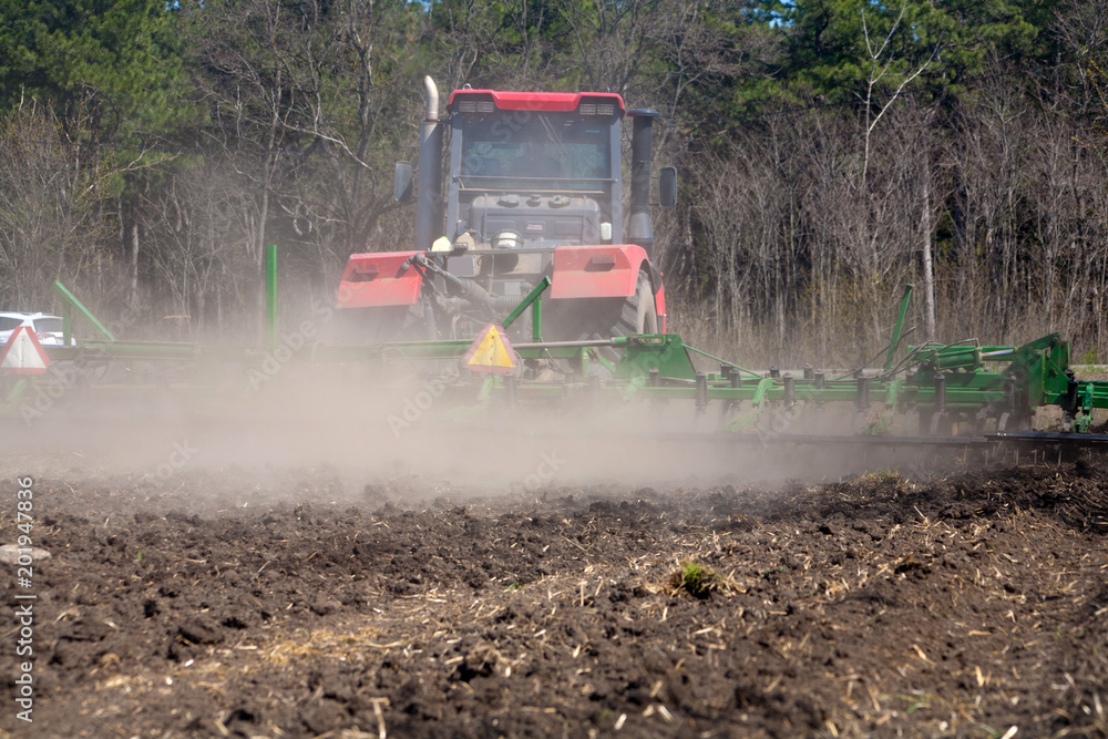 Fototapeta premium Rolnik w ciągniku przygotowuje ziemię z kultywatorem przedsiewnym
