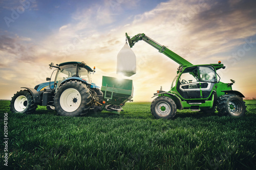 crane puts a sack of fertilizer on a trailer in the field in the spring photo
