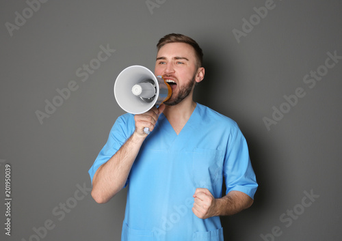 Obraz na plátně Male doctor shouting into megaphone on grey background