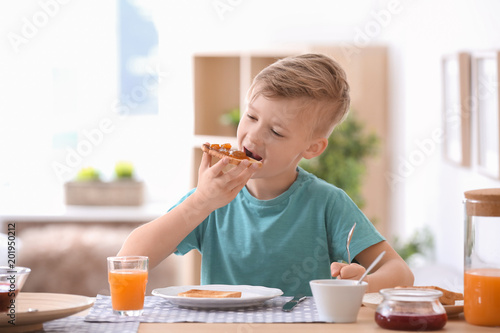 Cute little boy eating tasty toasted bread with jam at table
