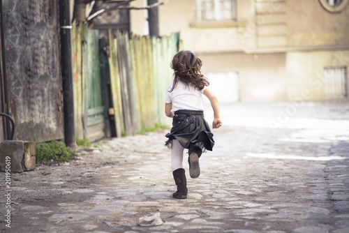 Obraz na płótnie Little girl running down a cobblestone alley