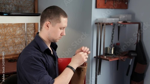 In the workshop, a man is sewing leather workpieces, making a wallet photo