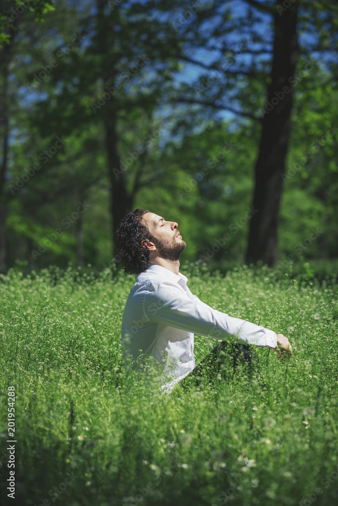 Young man practicing meditation and yoga focusing on a bright sunny day in a park surrounded by tall grass, serene and calm Young man practicing meditation and yoga focusing on a bright sunny day in a park surrounded by tall grass, serene and calm