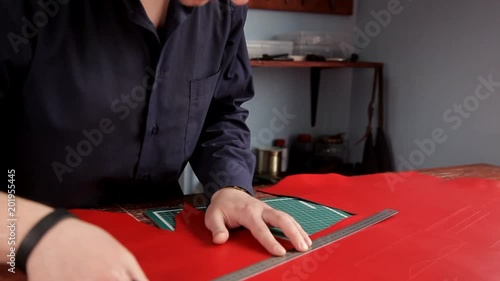 Сraftsman with an industrial knife and ruler cut blank skin of leather cloth photo