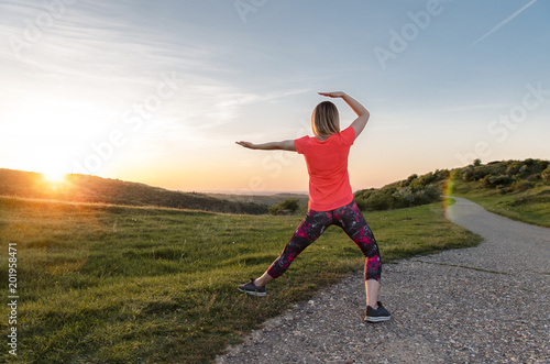 Back view, young woman doing Tai Chi in nature at sunset 