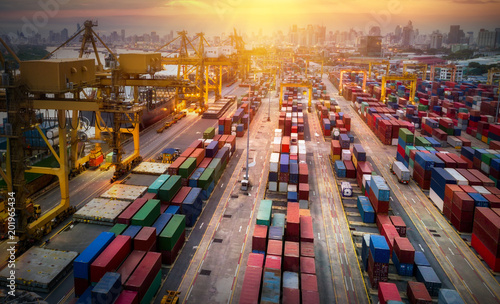 Aerial view from drone, Logistics and transportation of Container Cargo ship and Cargo plane with working crane bridge in shipyard at sunrise, logistic import export and transport industry background