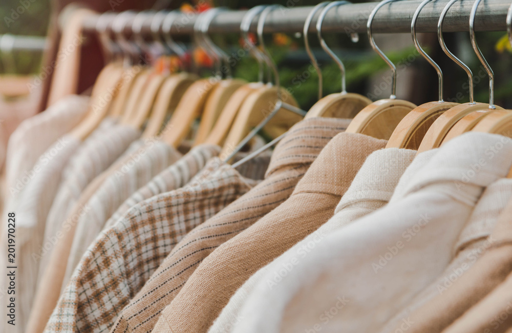 Obraz premium Clothes hang on wooden coat hangers in clothing store with nature tone.Soft focus.