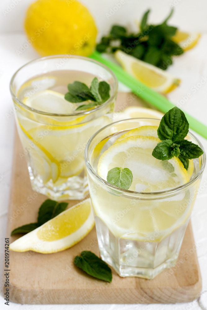 Lemonade with lemon slices, mint and ice and lemons on a light concrete background. Rustic style. Lemonade with lemon slices, mint and ice and lemons on a light concrete background. Rustic style.