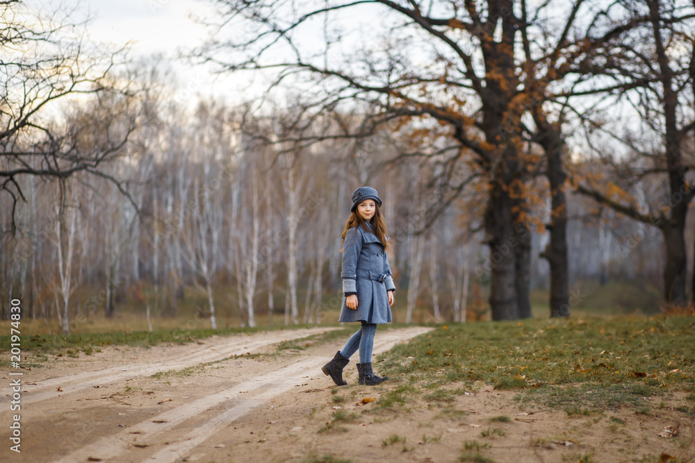 Obraz premium A cute girl in gey coat and gray hat in the oak wood in autumn walking at the sunset