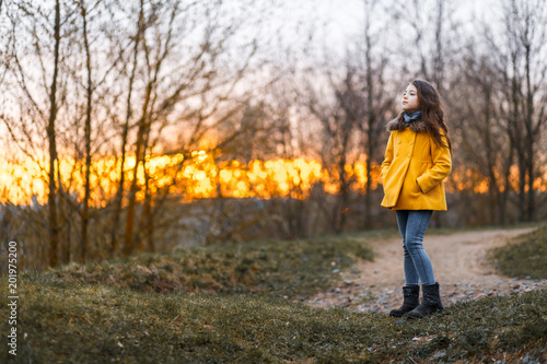 A little girl in a yellow coat walking in the wood at the sunset in a cold evening © Gorodetskaya