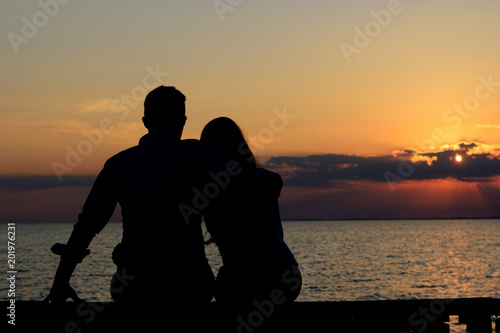 Two lovers (a guy and a girl) embrace and admire the cactin sitting on the bridge by the ocean. Love, romance, family, date. photo