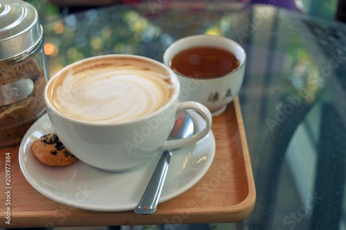 Latte coffee in a white cup with cookie and tea on a transparent glass table  