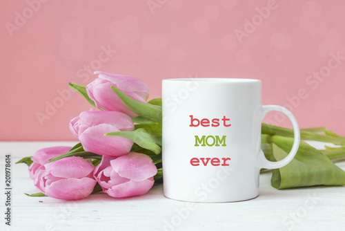 White coffee mug with Mothers Day greeting message and pink tulips on pink background.