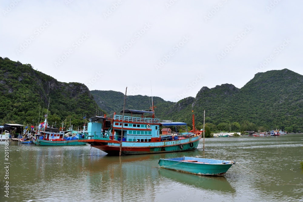 Fishing boats float in the water at the fishing village harbor with beautiful mountain in background at Ban Bangpu  , Khao Sam Roi Yot National Park , Prachuap Khiri Khan , Thailand
