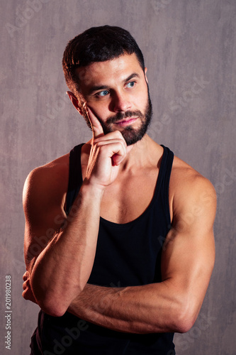 a muscular, healthy man in a black T-shirt thinks and plans an idea on a dark background. concept of a healthy body, sexuality and motivation © yurakrasil