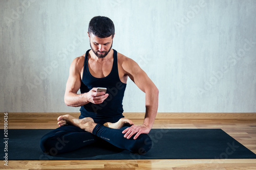 a man in dark sportswear practices yoga and makes selfie on a gray background. asana on the floor on yoga mats. the concept of concentration and possession of the body