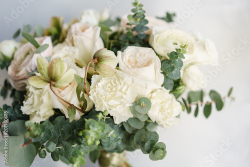 Fototapeta Naklejka Na Ścianę i Meble -  Wedding bouquet of white roses and buttercup on a wooden table. Lots of greenery, modern asymmetrical disheveled bridal bunch