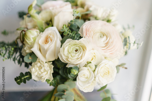Wedding bouquet of white roses and buttercup on a wooden table. Lots of greenery  modern asymmetrical disheveled bridal bunch