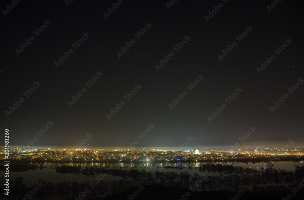 Starry night sky over the city and the river during spring flood. Landscape with a long exposure. Starry night sky over the city and the river during spring flood. Landscape with a long exposure.