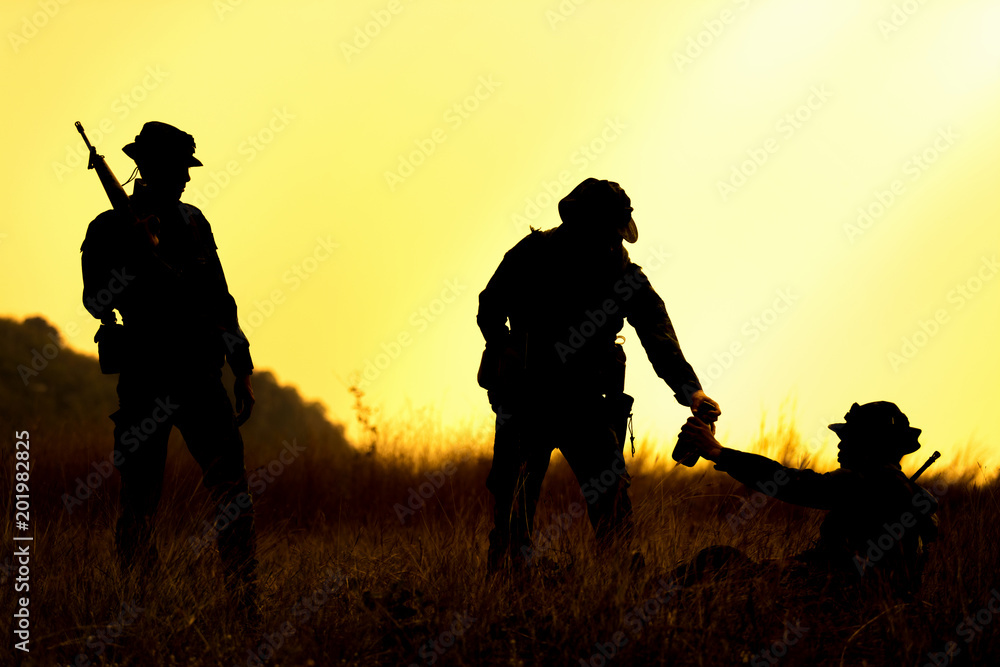 Silhouette of military soldier holding weapons overhead after get victory of war at sunset. Giving a flask to fellow.