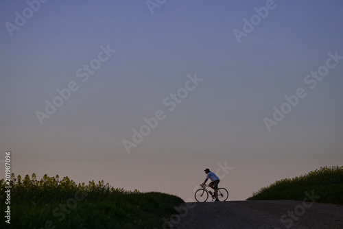 Cyclist on a road. Man with bike on a horizon at hot summer evening. 