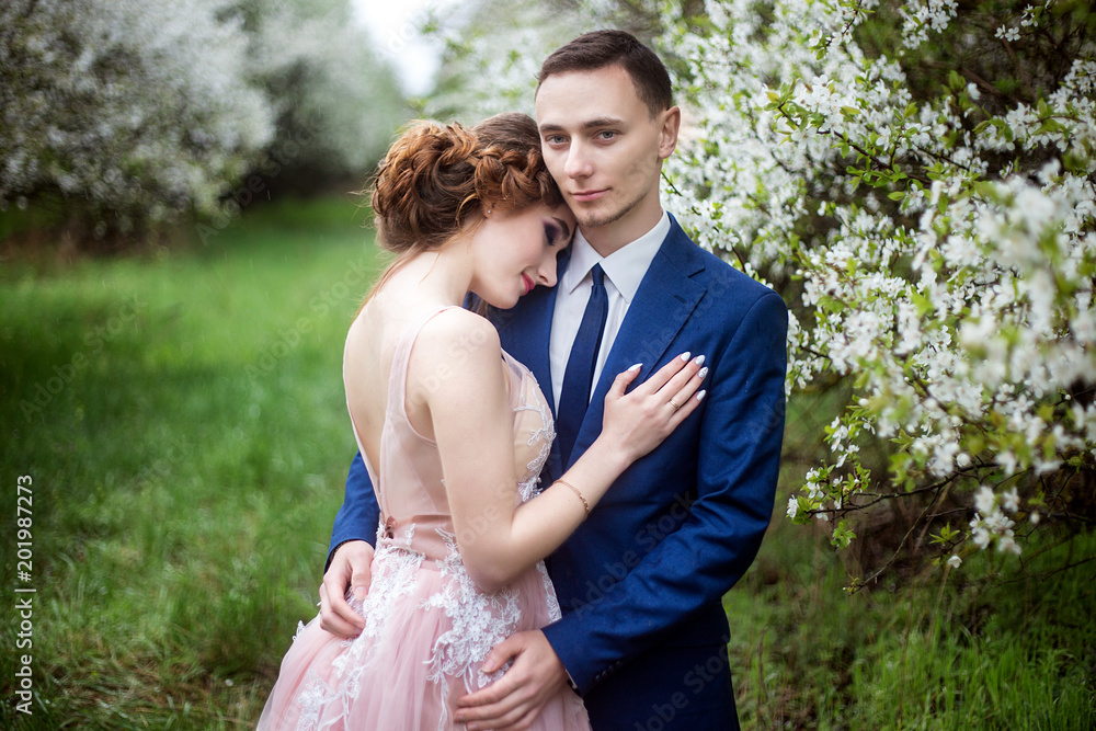 The bride and groom in wedding dresses against the backdrop of blooming gardens The bride and groom in wedding dresses against the backdrop of blooming gardens