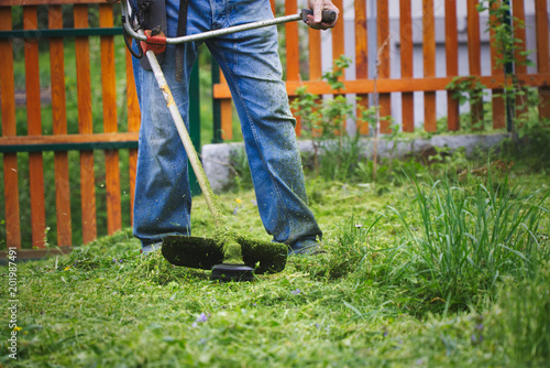 Gardener mowing grass by brushcutter in garden  photo