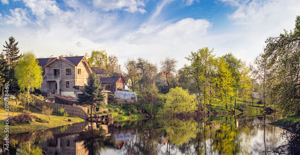 Panoramic vernal landscape with a house near the lake