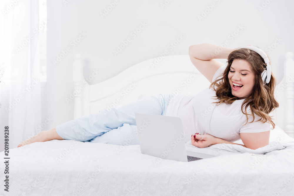 young woman in headphones using laptop on bed at home young woman in headphones using laptop on bed at home