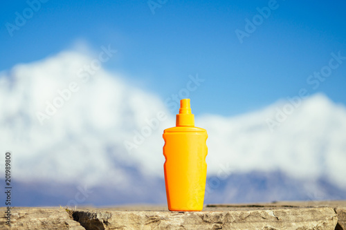 sunscreen in an orange bottle on a mountain background. the concept of preventing skin cancer and the use of sunscreen in the mountains. photo