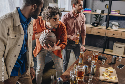 Canvas Print young multiethnic men playing with basketball ball and drinking beer together