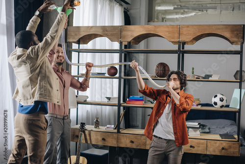 Photography happy multiethnic male friends having fun and drinking from beer bong together