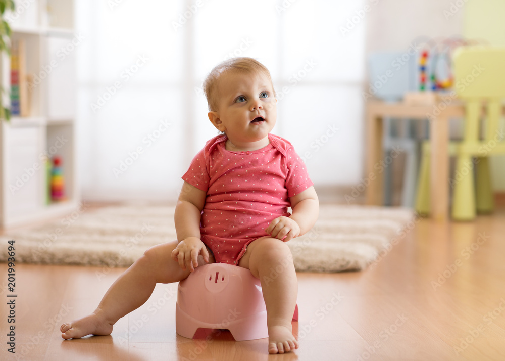 Baby girl one year old sitting on potty in home interior Baby girl one year old sitting on potty in home interior