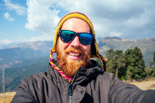 A young man with a red beard and a backpack in the mountains makes a selfie. the concept of active recreation and tourism in the mountains. Nepal in the spring