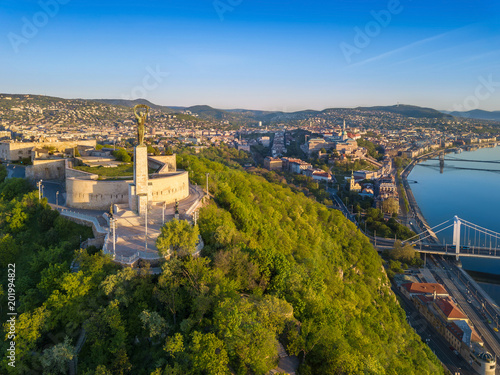 Budapest, Hungary - Aerial skyline view of Statue of Liberty on Gellert Hill at sunrise with clear blue sky. Buda Castle Royal Palace and Szechenyi Chain Bridge at background