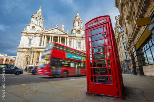 London, England - Traditional red telephone box with iconic red double-decker bus on the move at St.Paul's Cathedral on a sunny day
