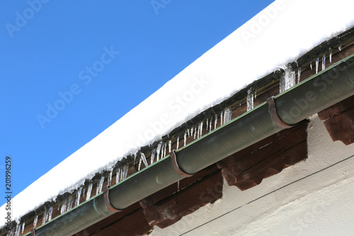 Gutter with icicles of ice on the roof after copious snowfall