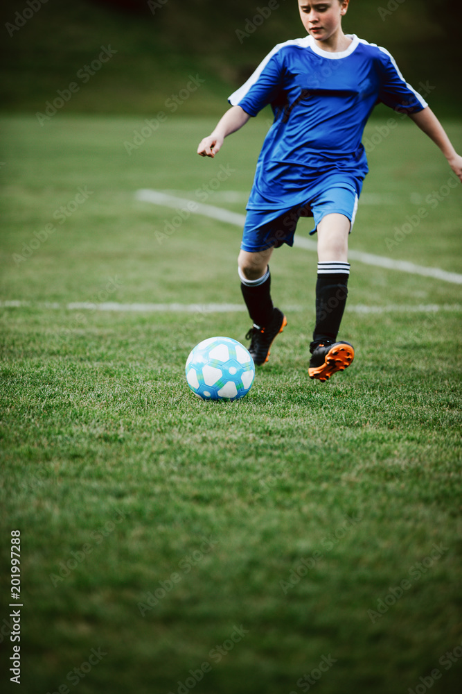 Teen girl playing soccer at local stadium outside on grass field kicking the ball. Children playing football, favourite sport, football fever worldwide. Teen girl playing soccer at local stadium outside on grass field kicking the ball. Children playing football, favourite sport, football fever worldwide.