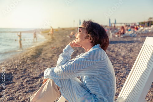 beautiful elderly woman sitting in a deckchair on the beach and admiring the sunset