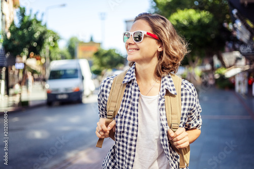Beautiful young woman in sunglasses with a backpack on the street background. Travel, freedom, youth, student life