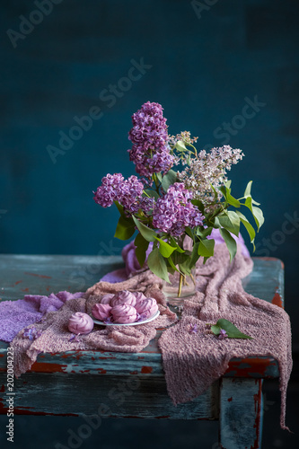Bouquet of lilac flowers and marshmallows on old vintage table. Still life on dark blue background.
