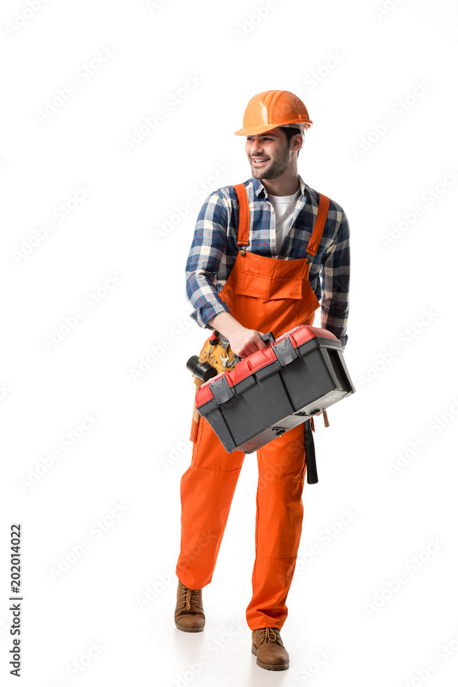 Smiling builder in orange overall and helmet carrying tool box isolated on white Smiling builder in orange overall and helmet carrying tool box isolated on white