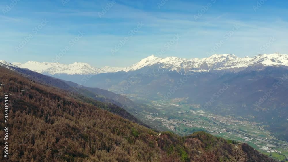 Aerial: drone flying over forest in springtime, aerial view of snow capped mountain range and valley on the Alps, clear blue sky, Turin, Italy Aerial: drone flying over forest in springtime, aerial view of snow capped mountain range and valley on the Alps, clear blue sky, Turin, Italy