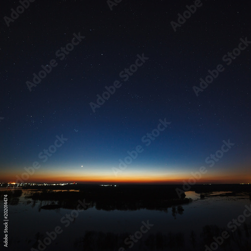 Night sky with stars above the river during the spring flood. View of the starry space. © olgapkurguzova