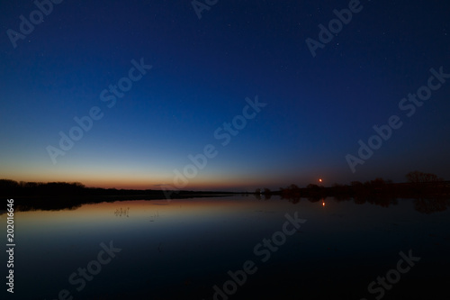 Sky with the stars before dawn. Night landscape with a lake.