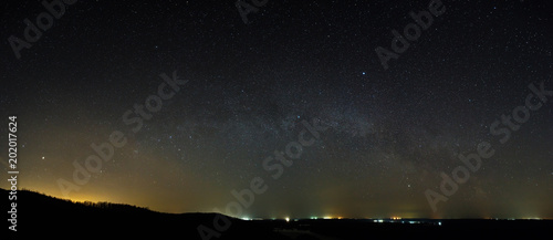 Stars of the Milky Way galaxy in the night sky above the skyline. Panoramic view of the starry space.