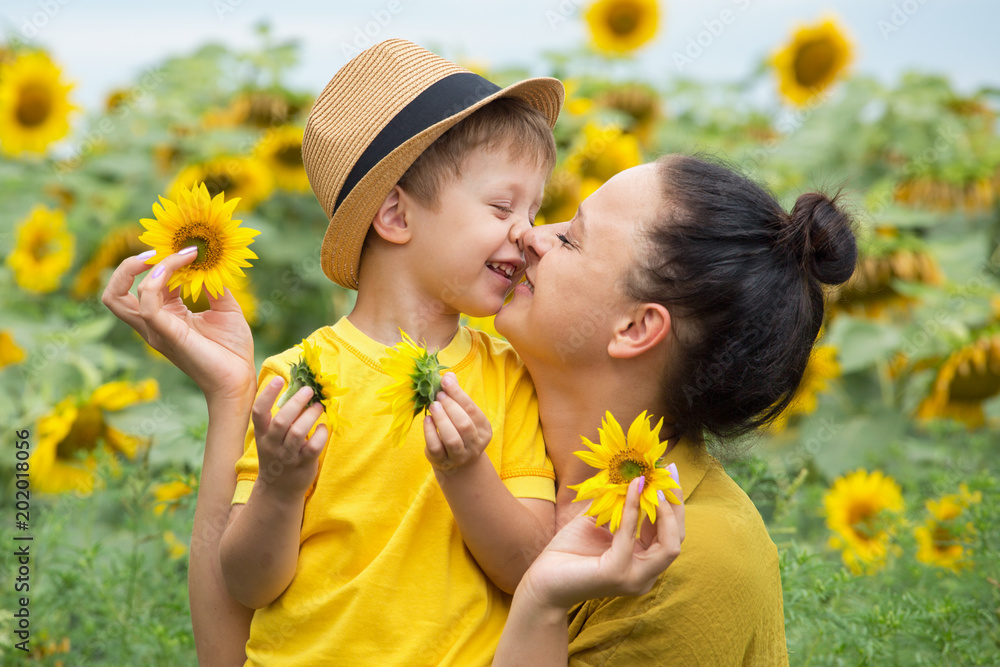 Mom and son hug, laugh and play in a field of sunflowers. Happy family moments spent in the open air. Mother's Day. Mom and son hug, laugh and play in a field of sunflowers. Happy family moments spent in the open air. Mother's Day.