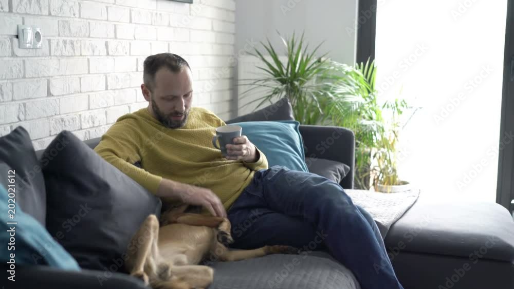 Young man drinking coffee, relaxing sitting on sofa with his dog
Young man drinking coffee, relaxing sitting on sofa with his dog
