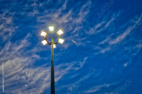 Lit hexagonal streetlight under dramatic sky.