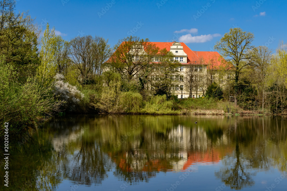 Frühling am Britzer Kirchteich in Berlin, im Hintergrund die Ostfassade der Alfred-Nobel-Schule